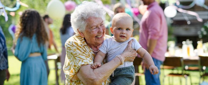 an elderly grandmother holding a baby grandchild at a party