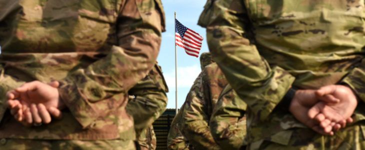 Soldiers lined up at parade rest in front of an American flag